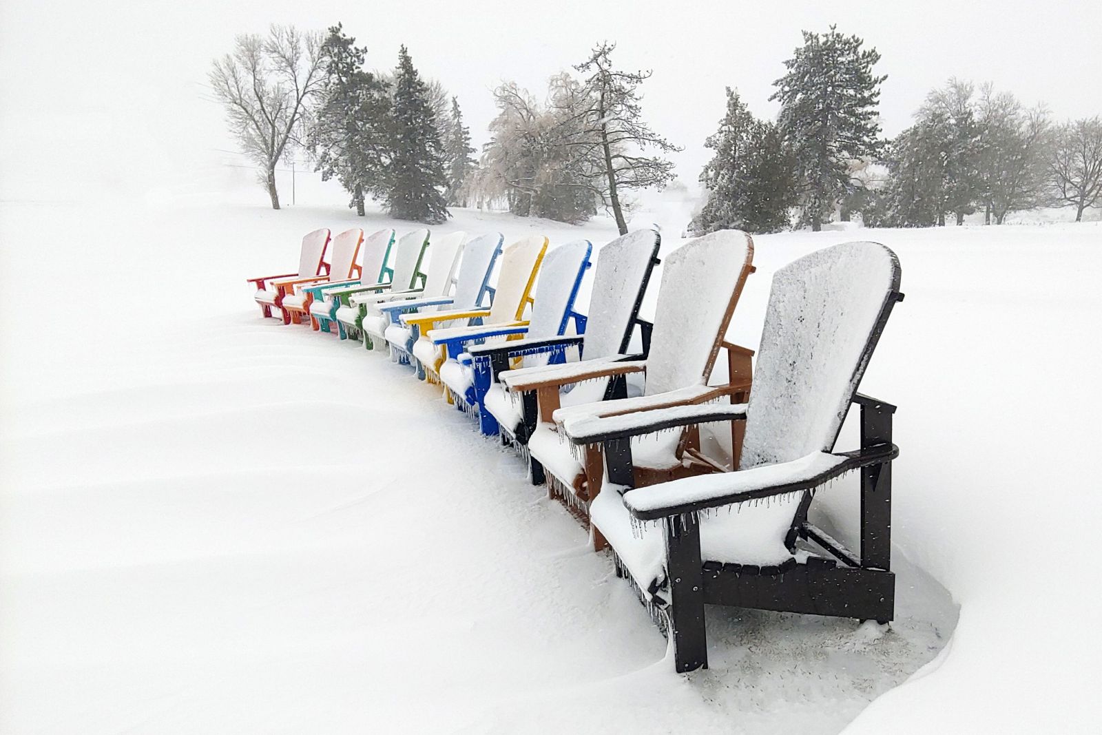 winter 2 Row of multicoloured recycled plastic Adirondack chairs lined up in snow – Mobek