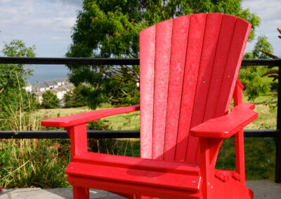 Red Mobek Adirondack chair on outdoor terrace with trees and hills in the background