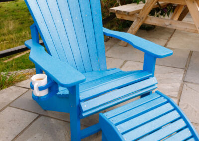 Blue Adirondack chair with matching footrest and white mug on paved patio – Mobek