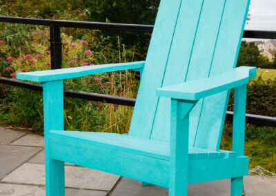 Teal Adirondack chair on outdoor terrace with green foliage backdrop – Mobek