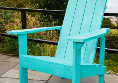 Teal Adirondack chair on outdoor terrace with green foliage backdrop – Mobek