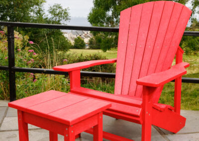 Red Adirondack chair with matching red side table on outdoor terrace with green foliage – Mobek