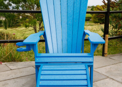 Blue Adirondack chair with footrest on paved patio surrounded by garden – Mobek